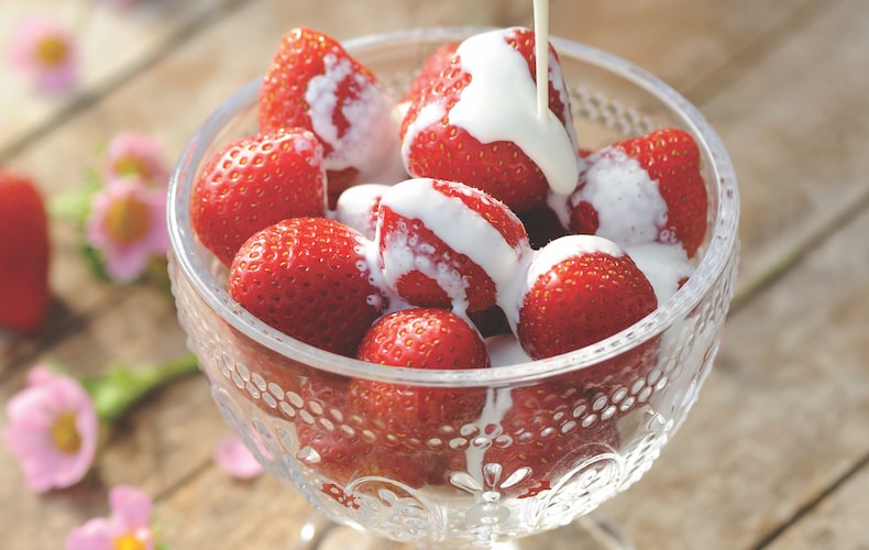 Strawberries in a glass bowl with pouring cream